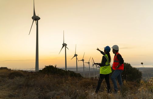 maintenance engineer team working in wind turbine farm at sunset